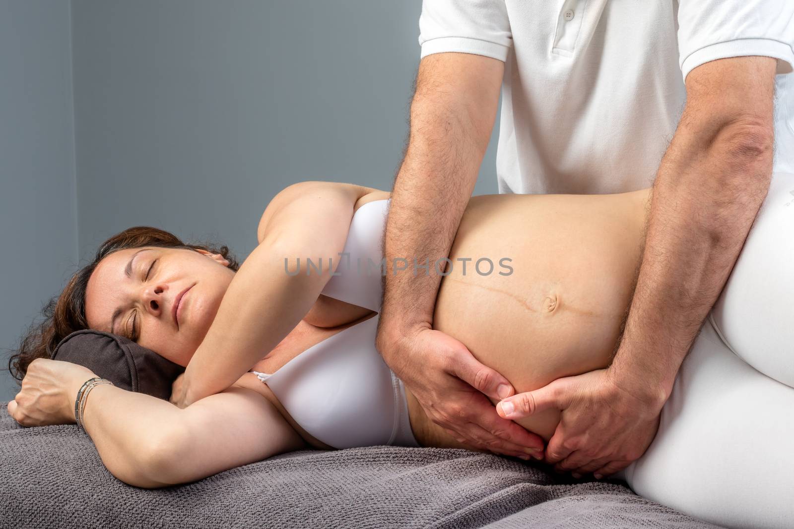 Close up portrait of pregnant woman receiving osteopathic treatment on tummy.