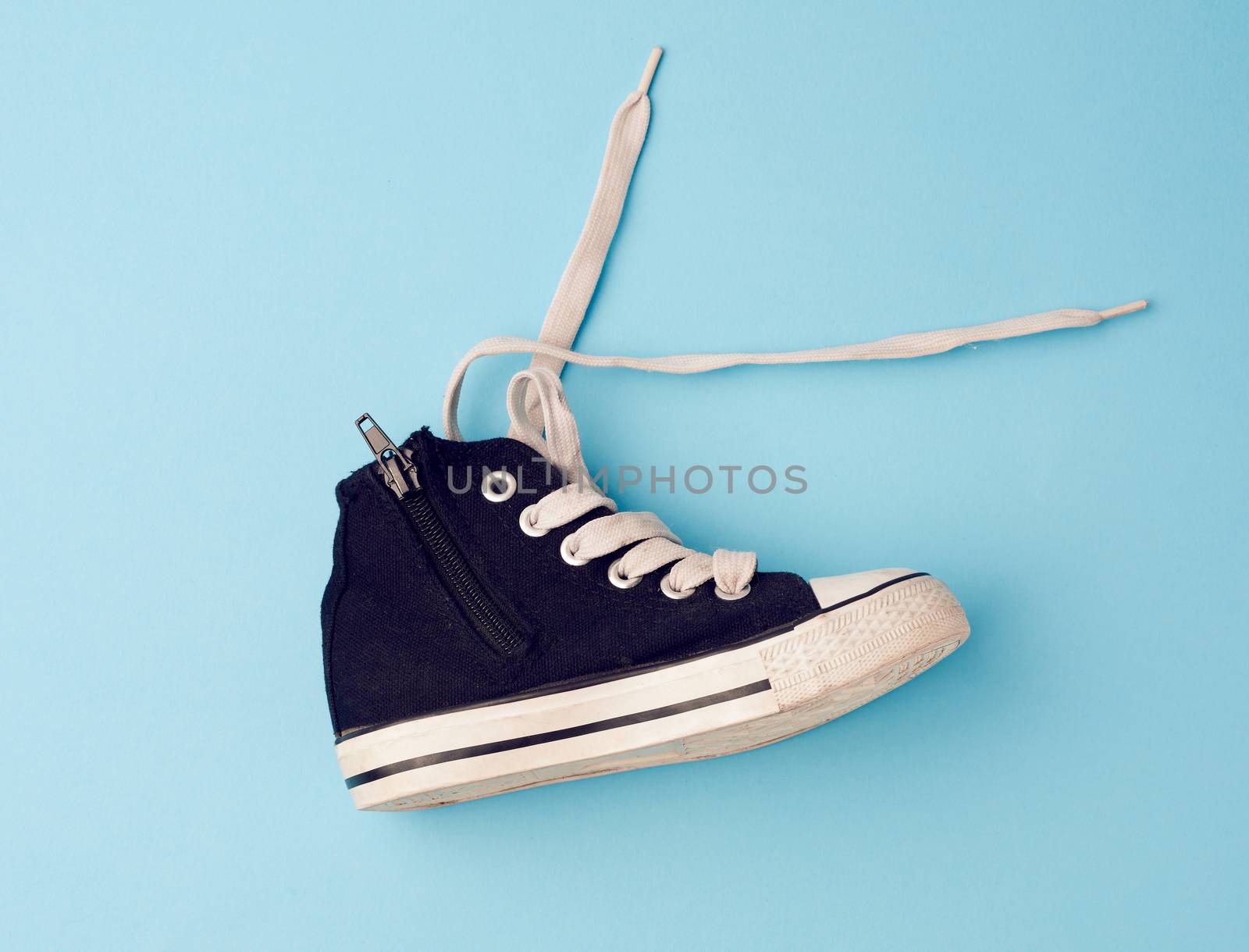 children's black textile sneaker with rubber sole and with white laces, blue background