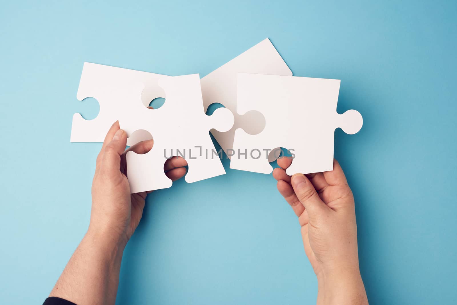 two female hands holding big paper white blank puzzles on a blue background, concept of business