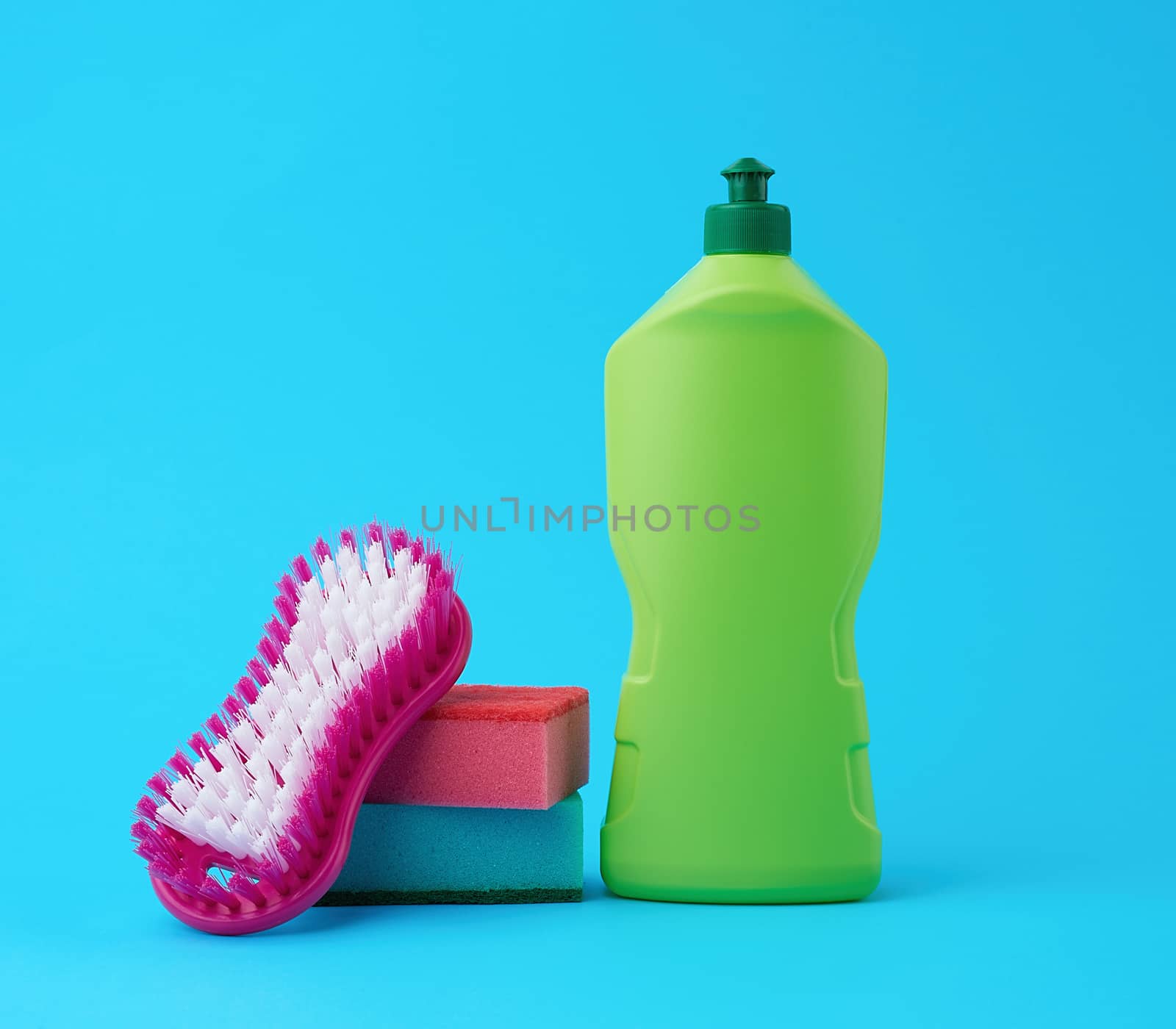 multicolored kitchen rectangular dishwashing sponges and green plastic bottle with detergent, blue background