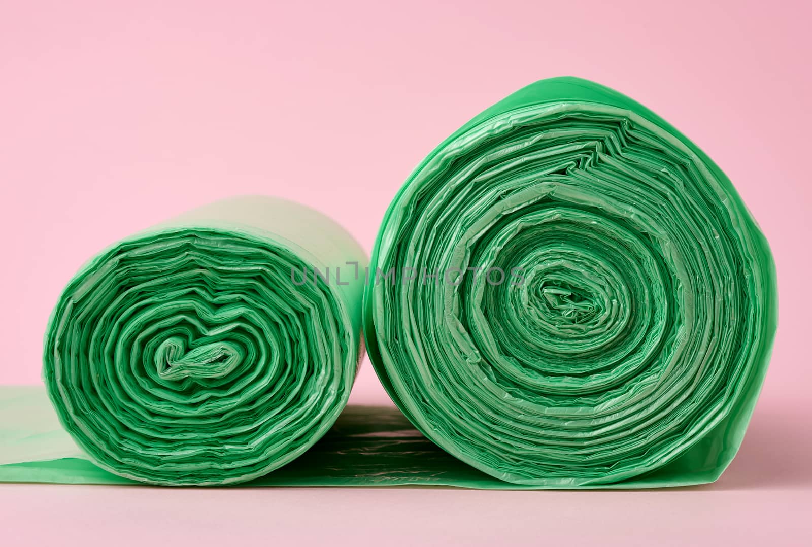 two rolls green plastic bags for trash bin on pink background, close up