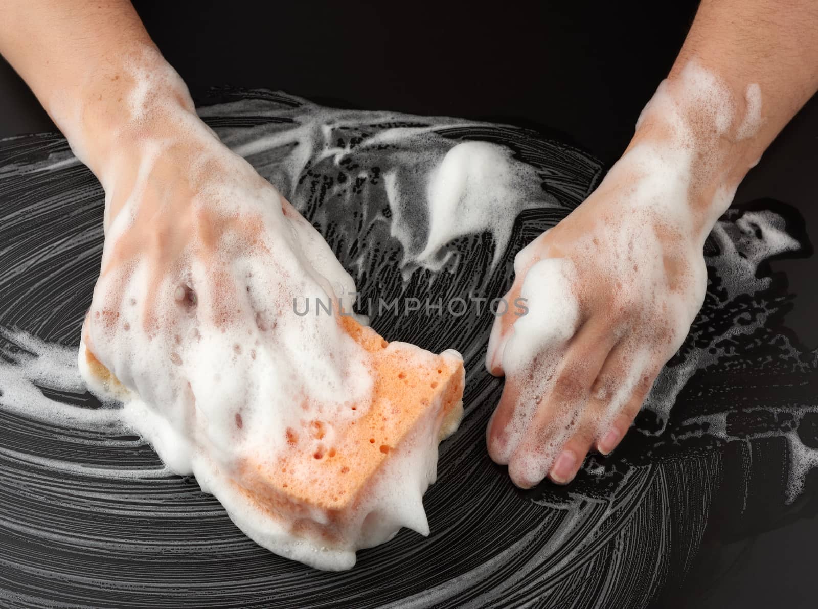 two female hands in white soapy foam hold a wet sponge and wipe the black surface, concept of cleaning and washing surfaces, top view