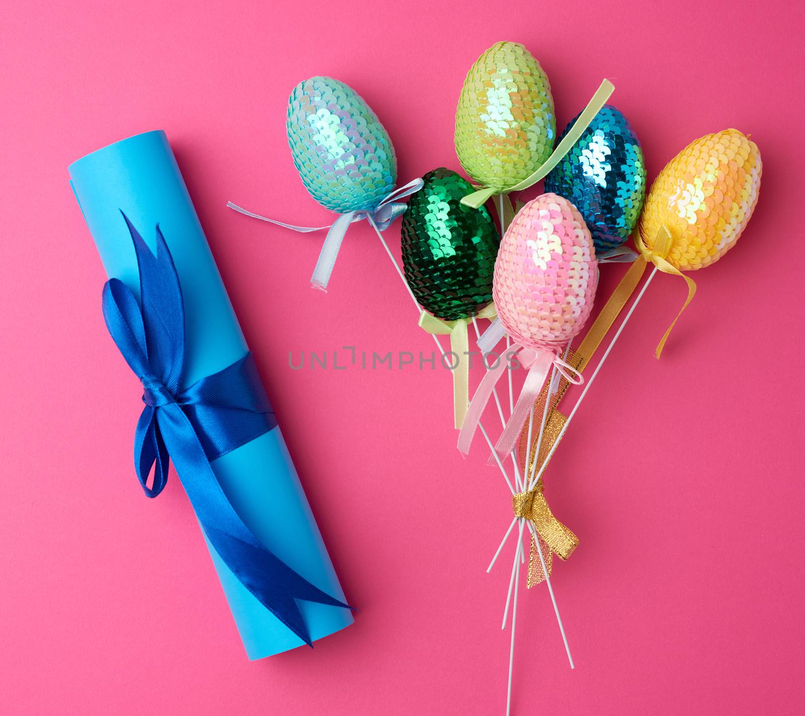multicolored decorative Easter eggs decorated with sequins and blue paper scroll on a pink background, festive backdrop, top view