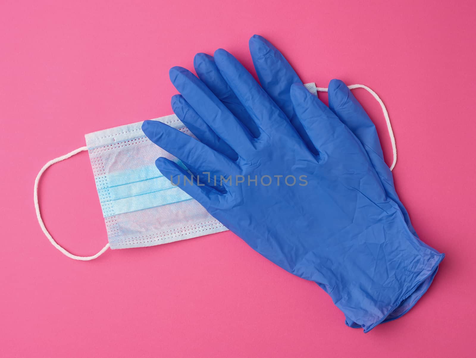 disposable gloves and medical mask made of non-woven material with white rubber bands on a pink background, protective accessory for the respiratory tract from the virus