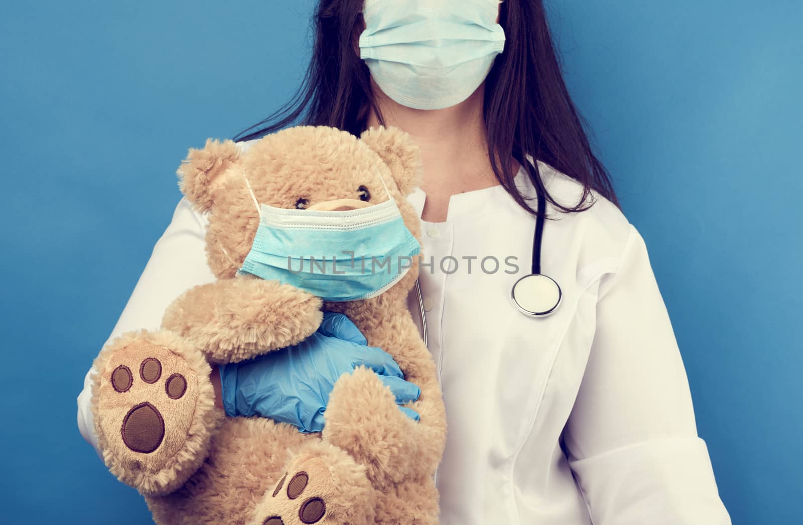 woman doctor pediatrician holds brown teddy bear in hand in white medical disposable mask, concept of preventing epidemics and pandemics against flu