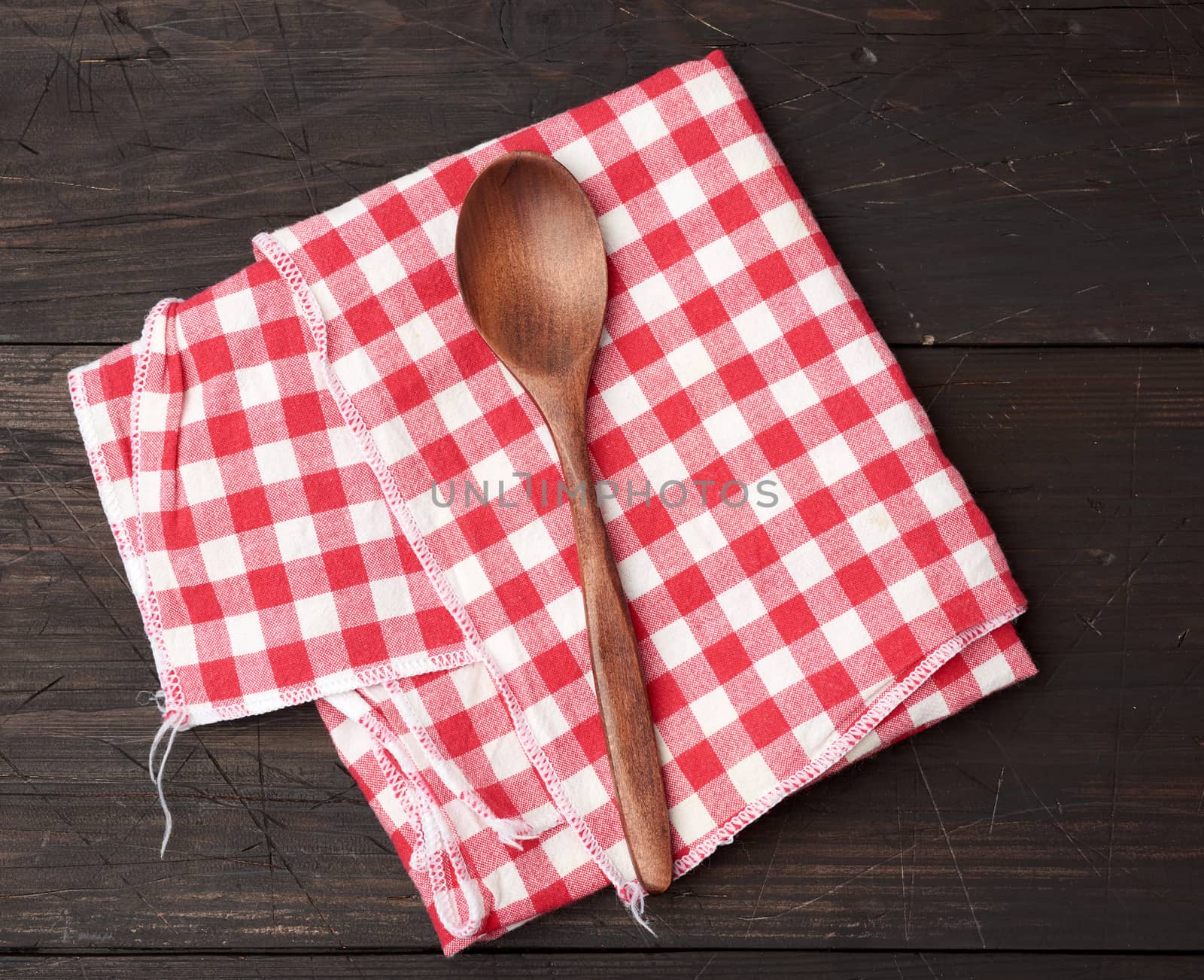wooden spoon and red textile kitchen towel on brown wooden background, top view