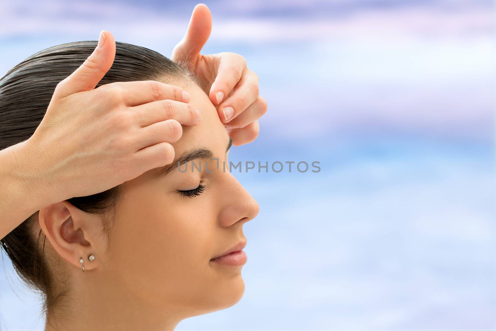 Therapist doing alternative healing on young woman. Reiki therapist touching energetic area on forehead.