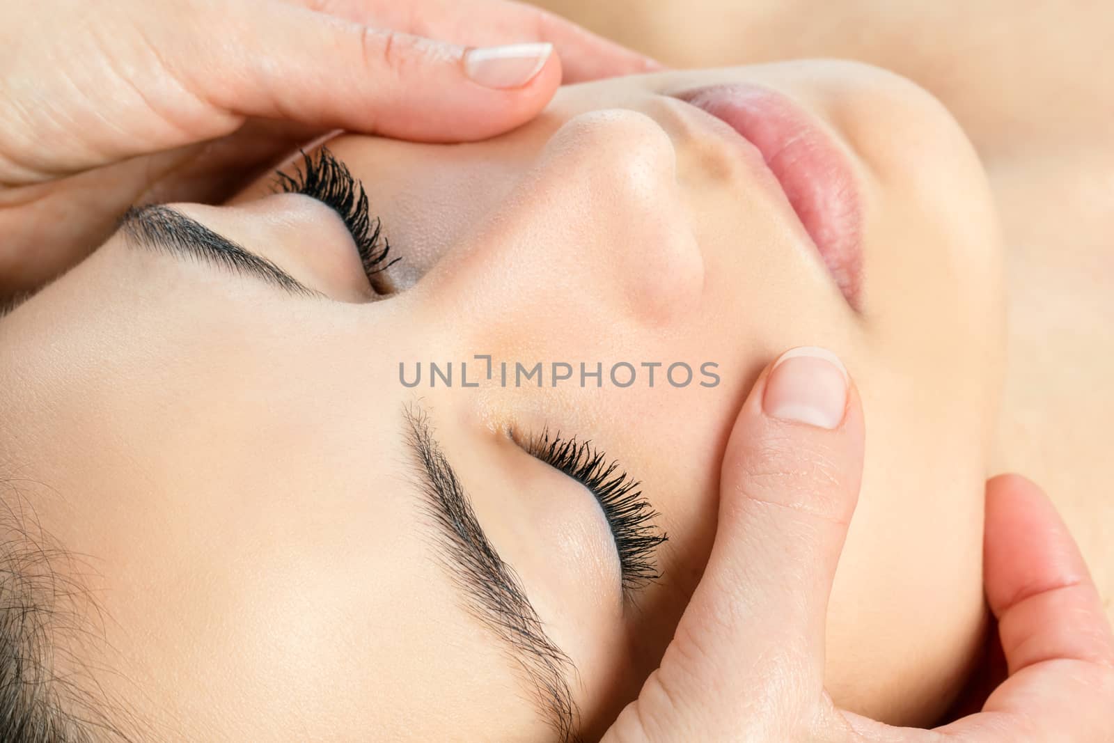 Extreme close up face shot of attractive woman having facial massage.Therapist massaging cheeks.