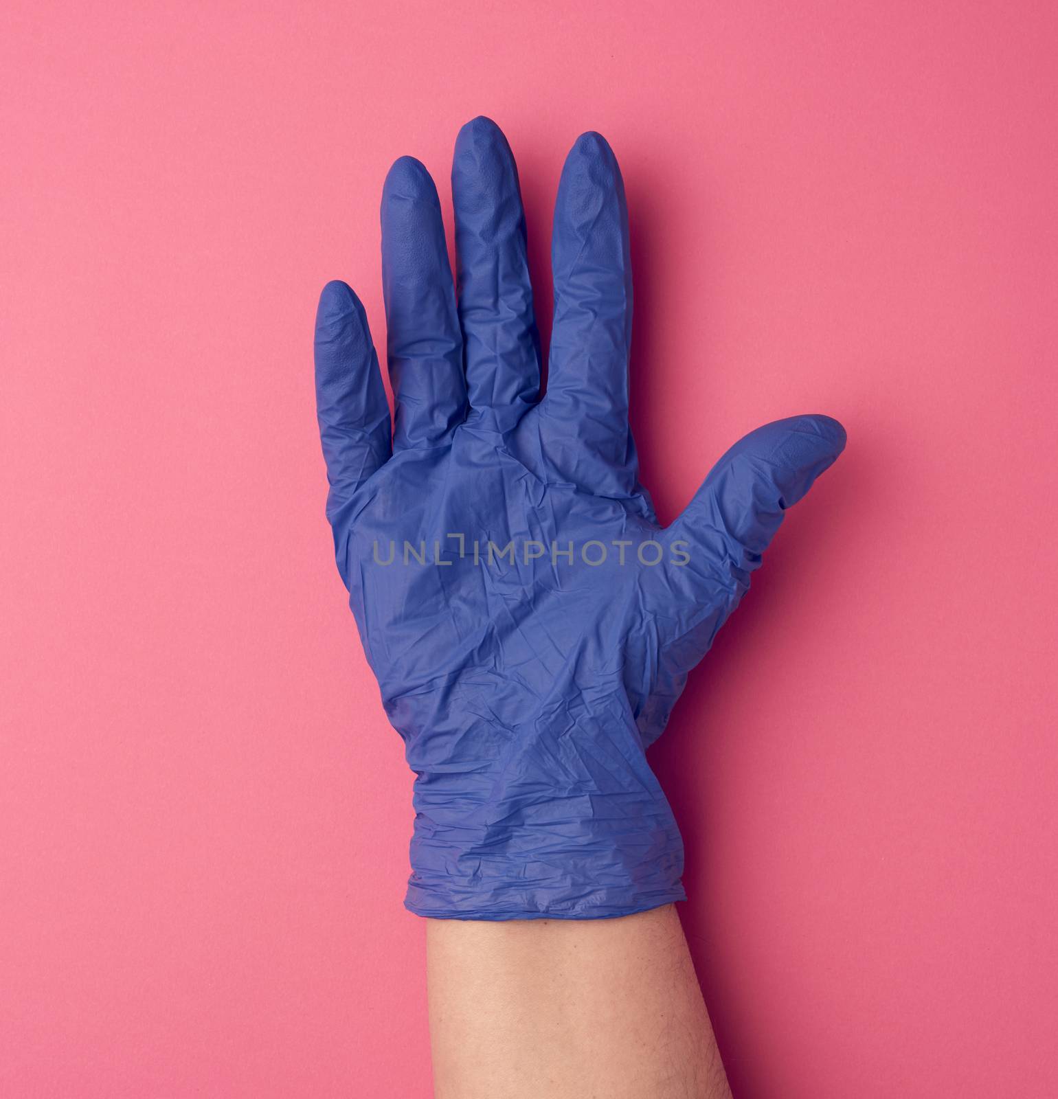 blue medical glove is worn on the arm, part of the body on a pink background, close up