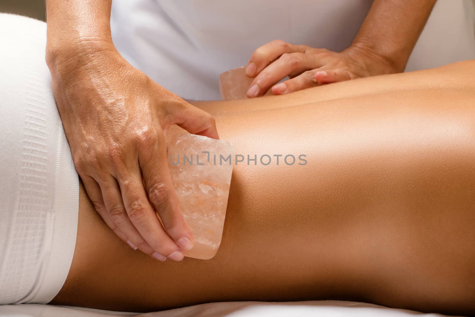 Close up detail of himalayan salt stone massage. Therapist massaging lower back of woman with hot salt brick.