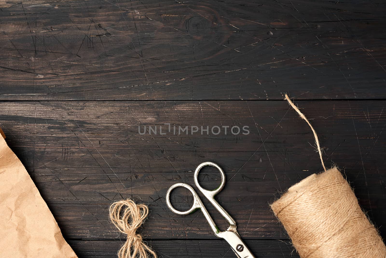 brown thread twisted into a spool and vintage metal scissors on a wooden background from boards, place for an inscription