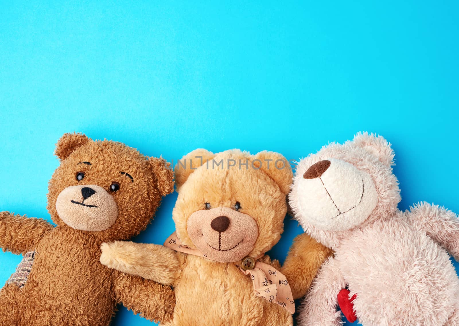 various teddy bears lie on a blue background head to head and look up, concept of friendship and mutual assistance, copy space