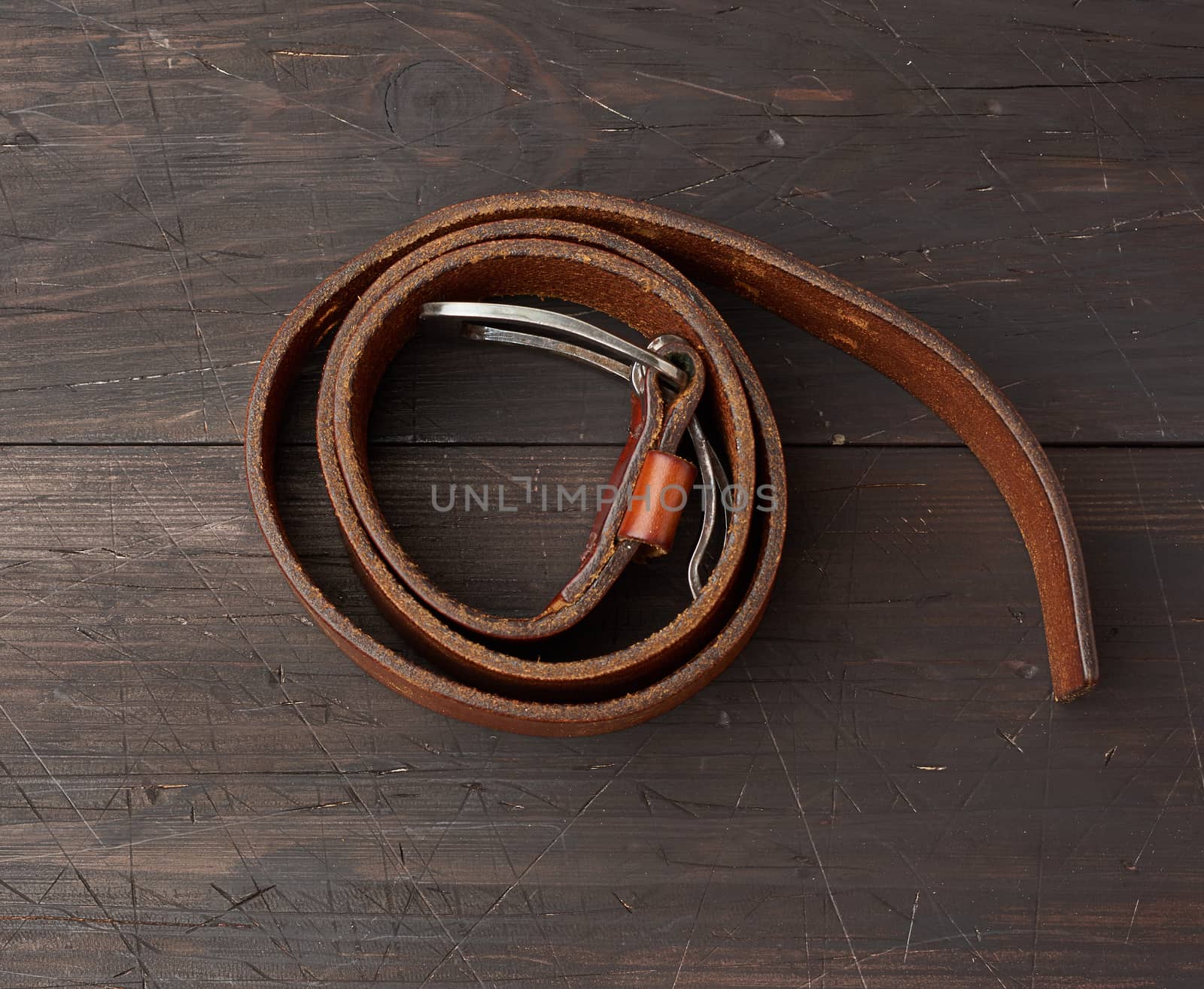 brown leather men's belt with metal buckle on a wooden background, top view