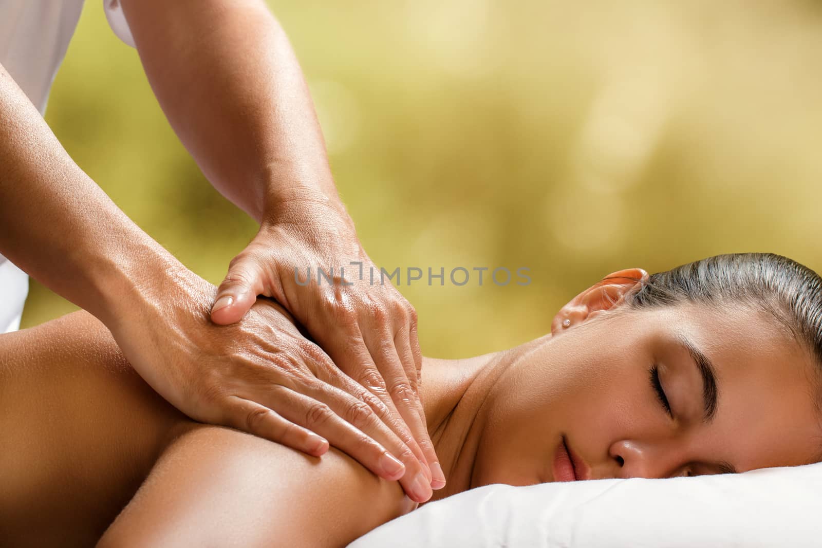 Close up of therapist doing neck massage on woman in spa against colorful green background.