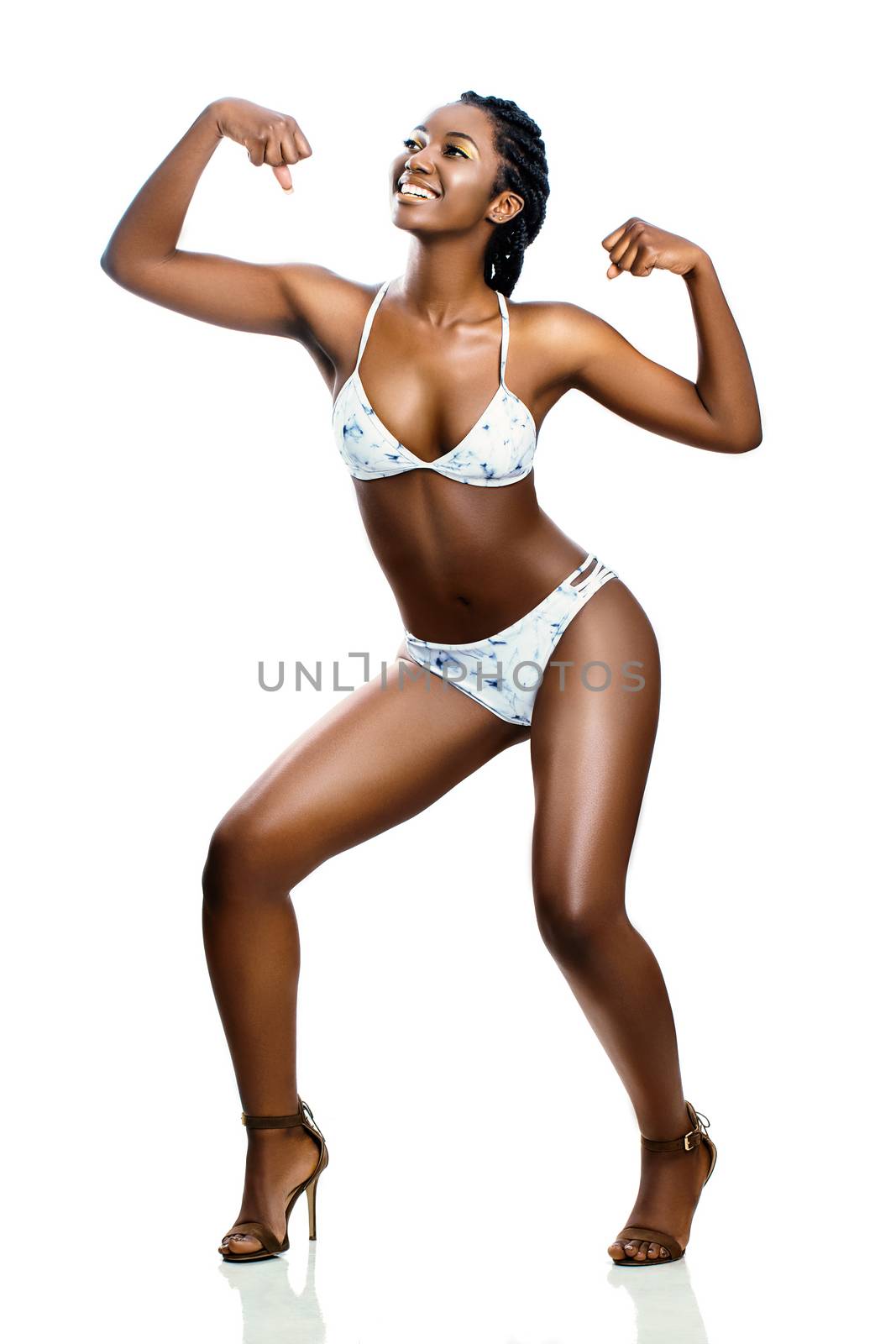 Full length studio portrait of attractive young african woman in bikini. Smiling girl showing muscles raising arms. Isolated on white background.