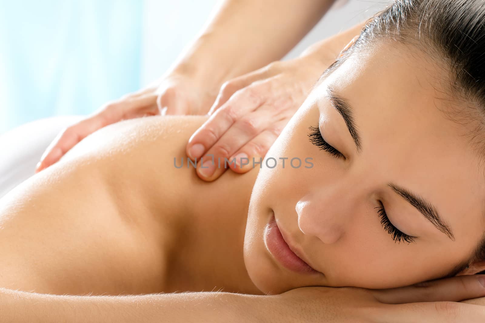 Close up portrait of young woman relaxing in spa.Therapist doing back massage on girl in background.