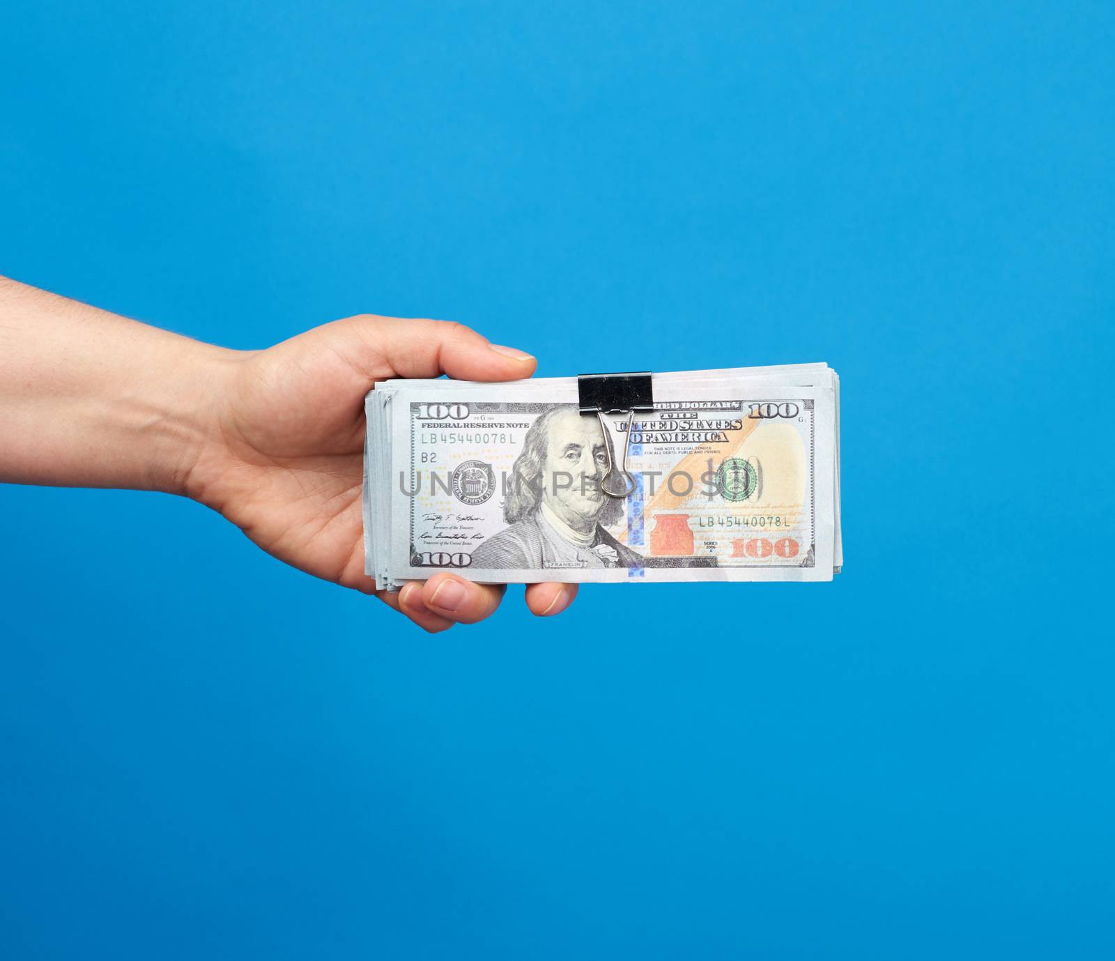 female hand holds a stack of paper American dollars on a blue ba by ndanko