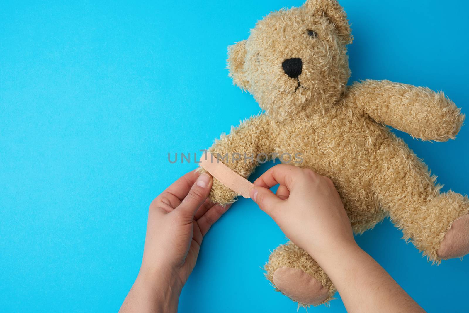 two hands holding a teddy bear and gluing an adhesive plaster on by ndanko