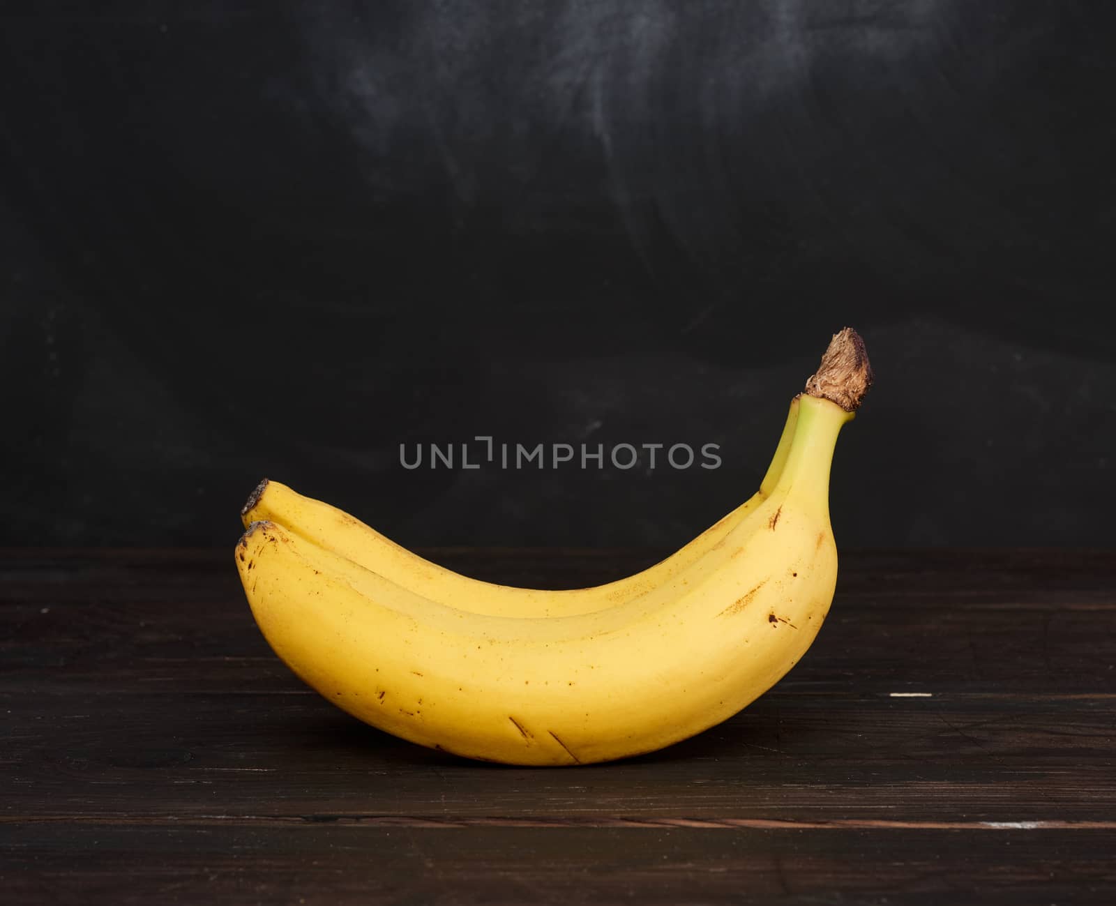 bunch of yellow unpeeled ripe bananas on a brown wooden table by ndanko