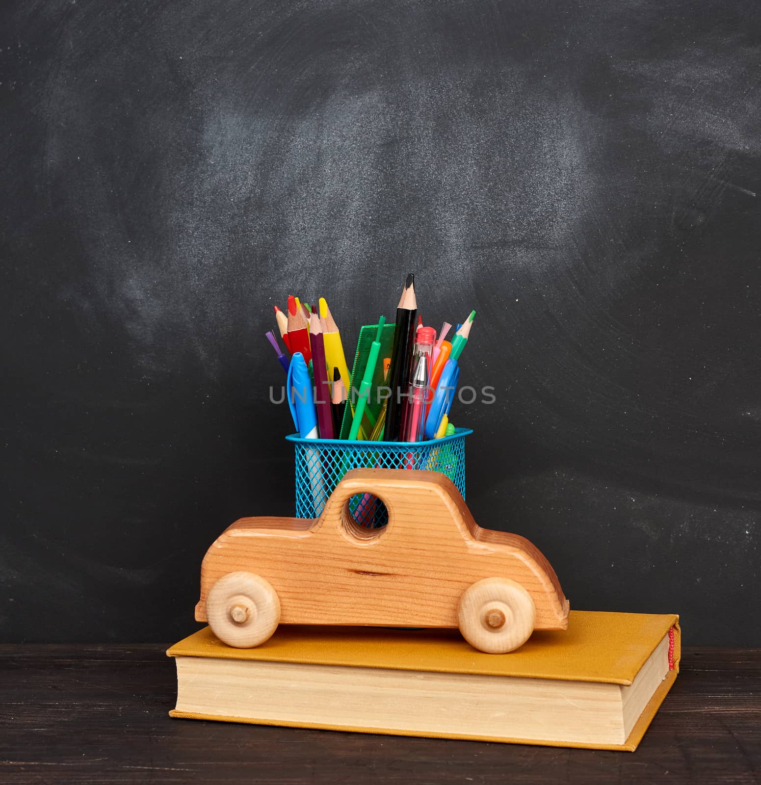 wooden toy, book, multicolored pens and pencils and other stationery in a blue metal holder, black background, back to school 