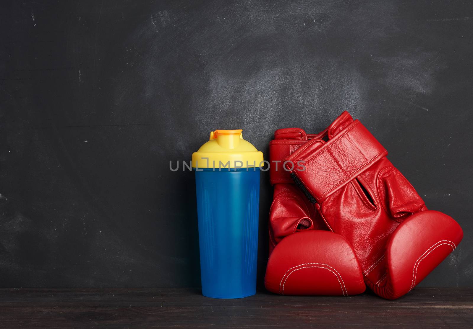 pair of red leather boxing gloves and blue plastic bottle on a black background, sports equipment, copy space