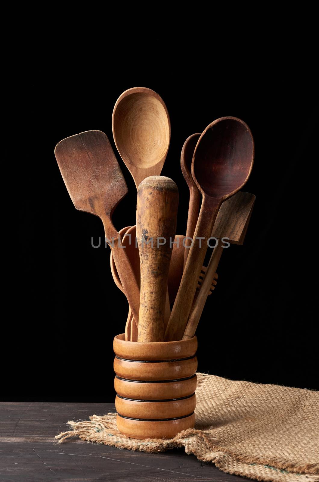 various spoons and kitchen wooden utensils in a bowl on the table, black background