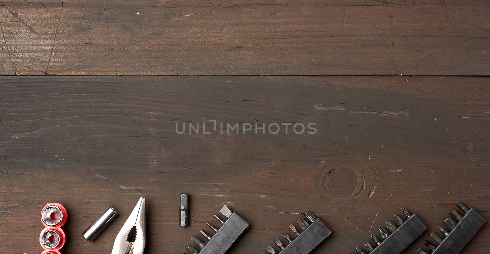 metal pliers and various nozzles on a brown wooden background, top view, copy space