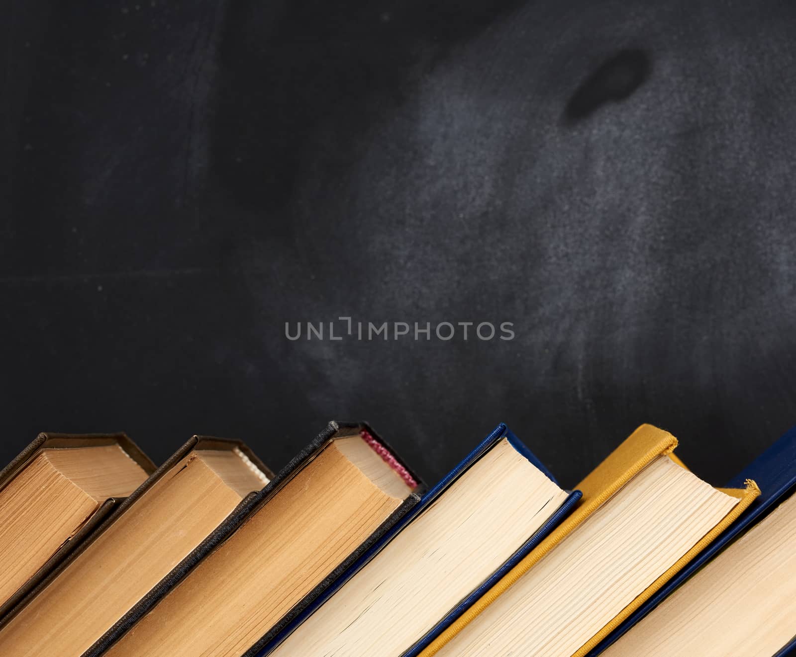 stack of various books on the background of an empty black chalk board, place for text, back to school