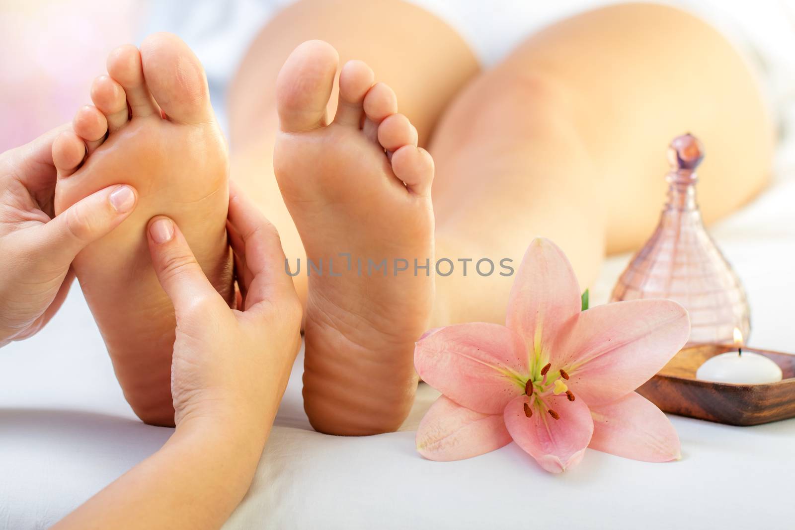 Close up of hands doing foot reflexology massage on female foot. Flower, candle and massage oil next to feet.