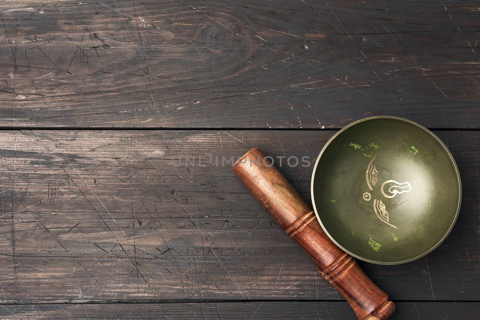 Tibetan singing copper bowl with a wooden clapper on a brown wooden table, objects for meditation and alternative medicine, top view, copy space