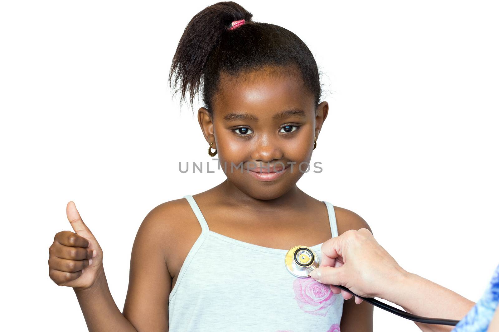 Close up portrait of cute little african girl having heartbeat taken.Hand positioning stethoscope against chest.Kid doing thumbs up Isolated on white background.