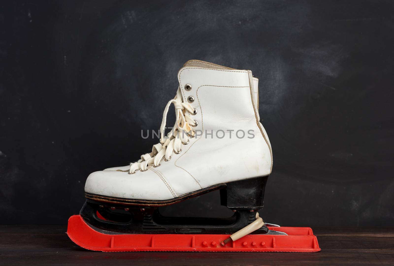white leather skates for figure skating stand on a brown wooden background, sports equipment