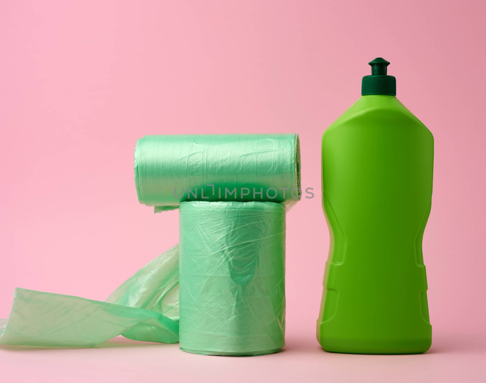 roll with transparent bags for the bin and a plastic bottle with detergent on a pink background