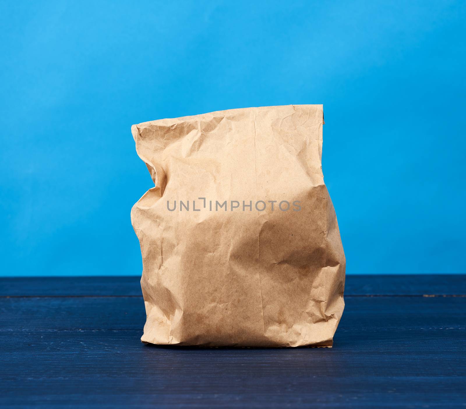 full paper disposable bag of brown kraft paper on a blue background, concept of rejection of plastic packaging, template for designer, packaging for contactless product delivery