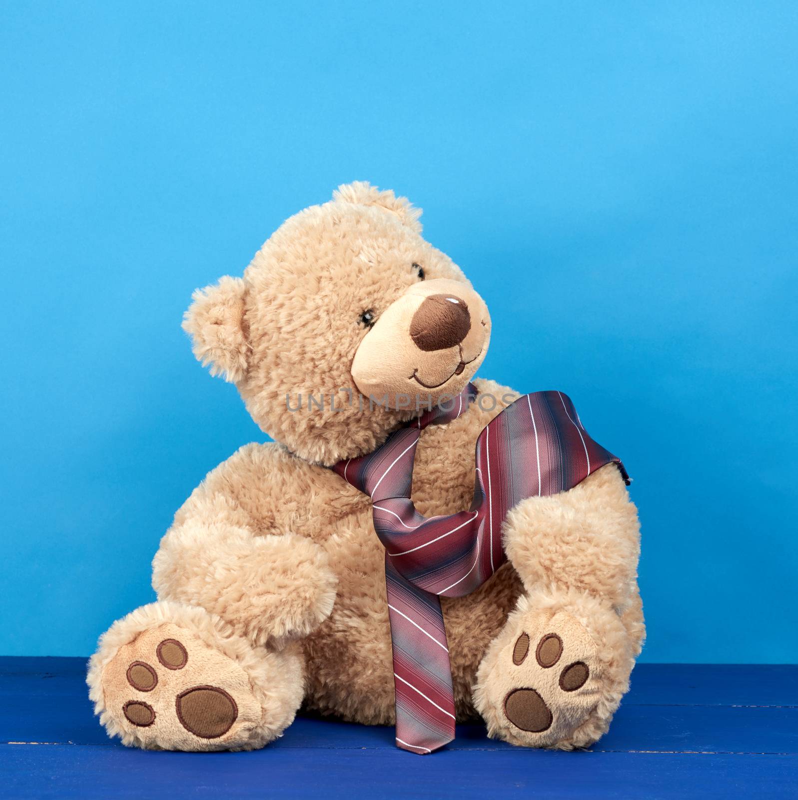 brown teddy bear sits on a blue wooden background, a tie is tied around his neck, dad bear