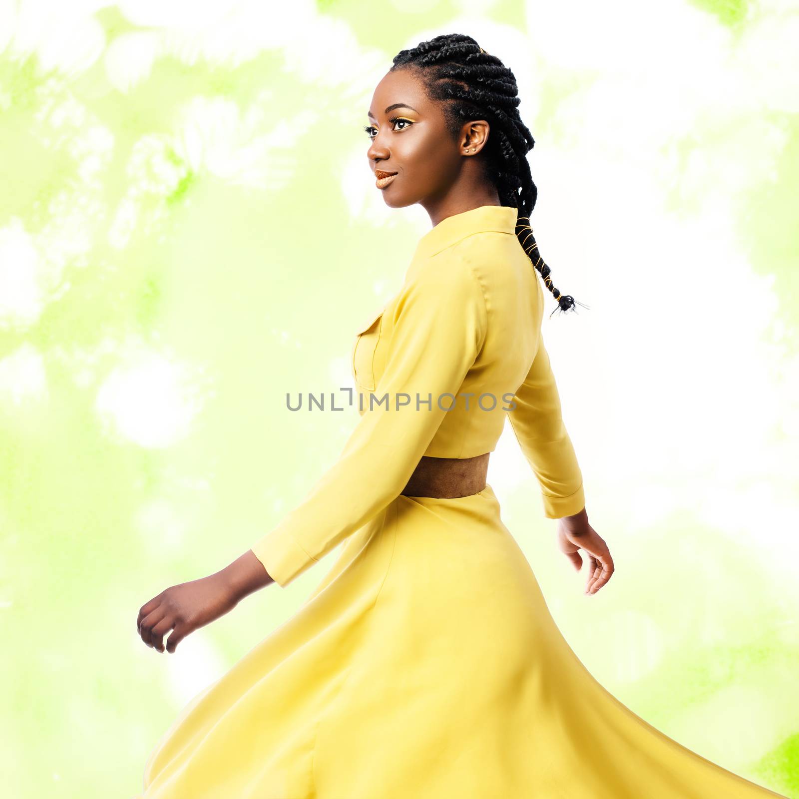 Close up studio portrait of young attractive african woman in yellow dress.Girl with braided hairstyle swaying silky dress against colorful green background.