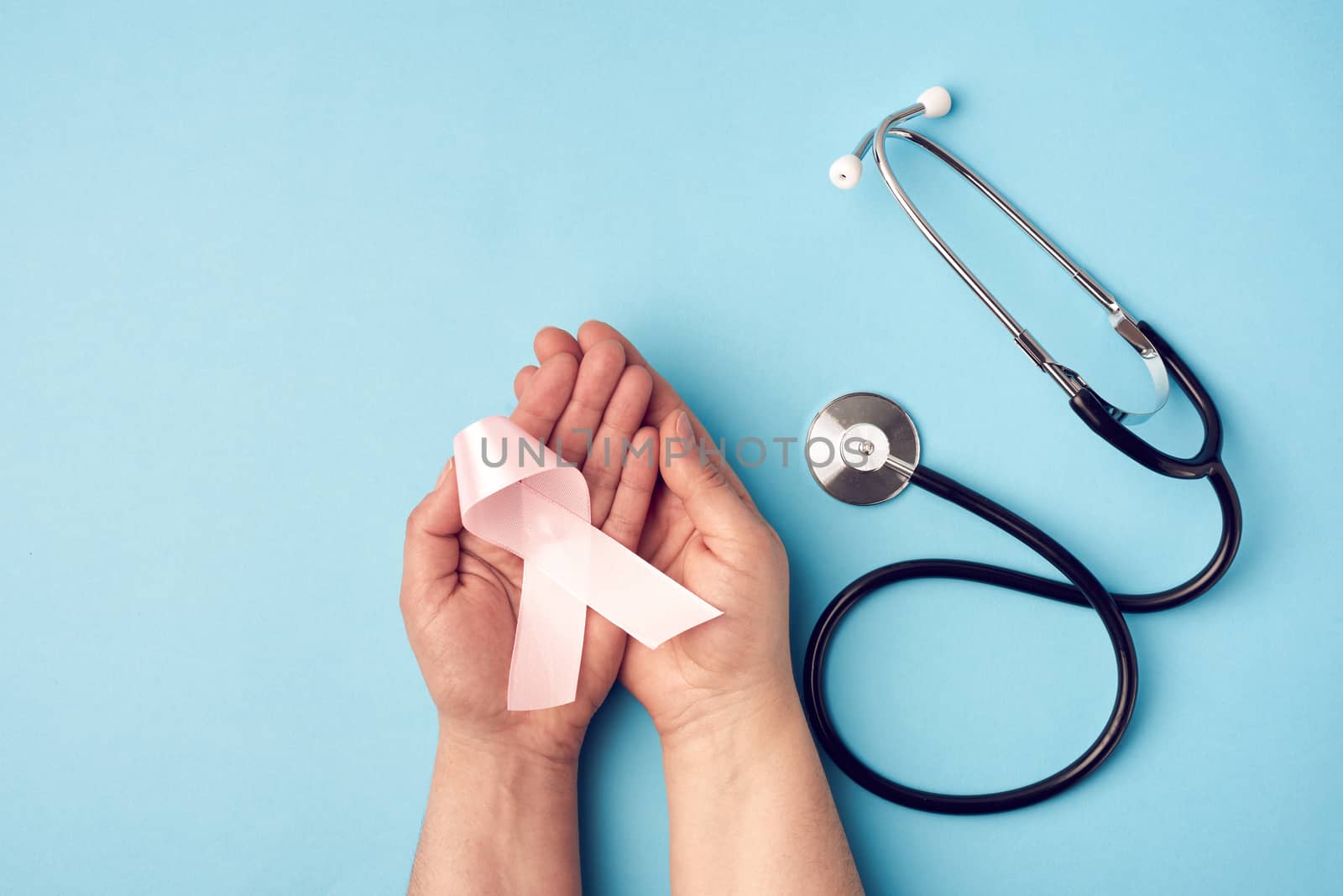 female hand holds a pink bow-shaped ribbon on a blue background by ndanko