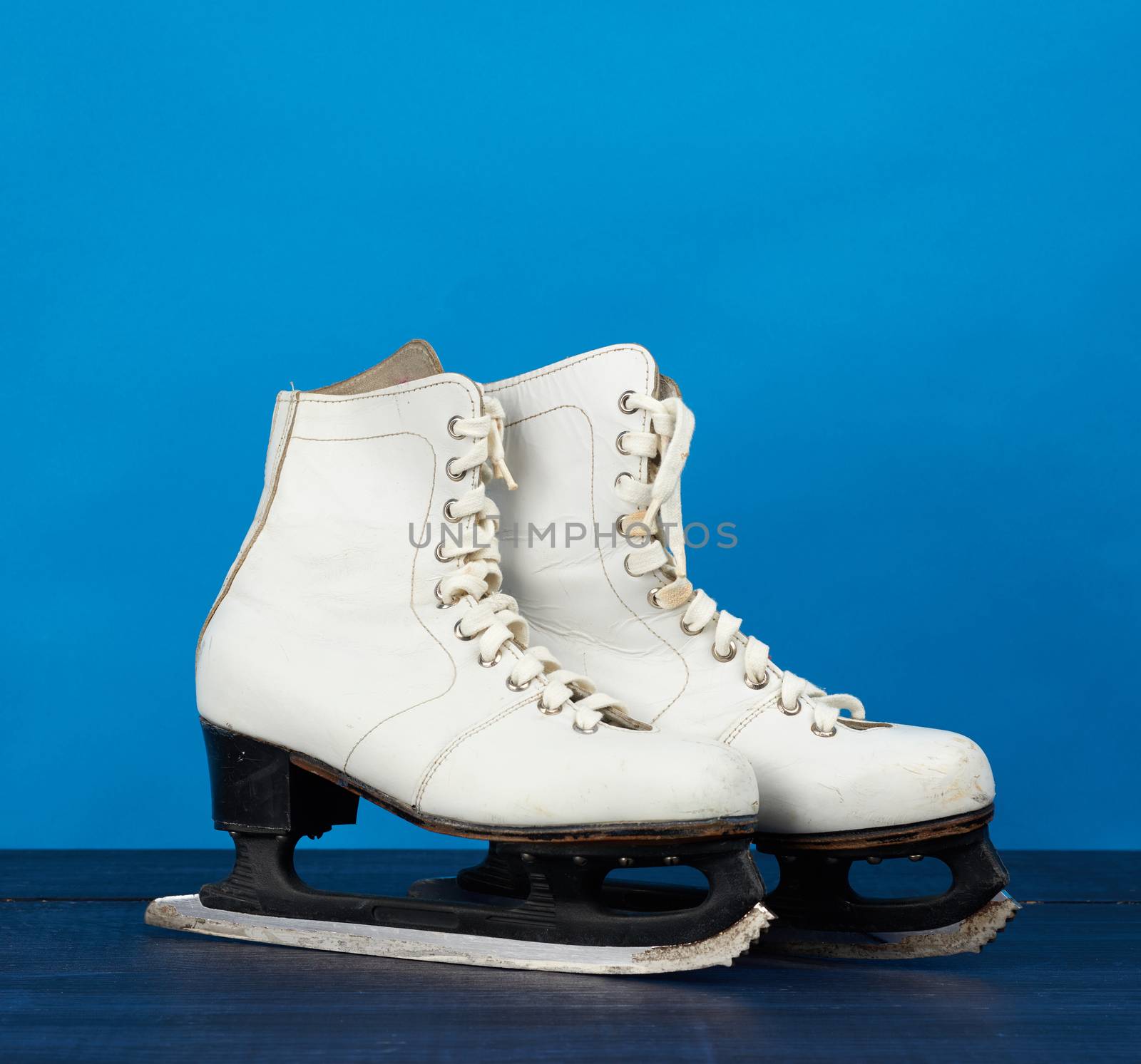 white leather skates for figure skating stand on a blue wooden b by ndanko