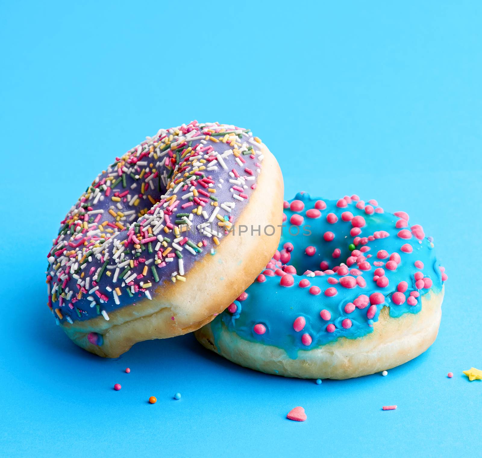 two round baked donut with colored sugar sprinkles and with blue by ndanko
