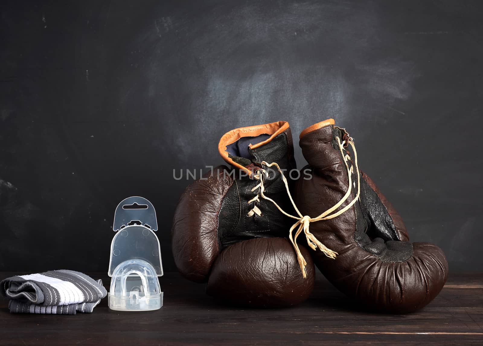 pair of brown leather vintage boxing gloves, silicone cap and wrist bandage, wooden background, sports equipment
