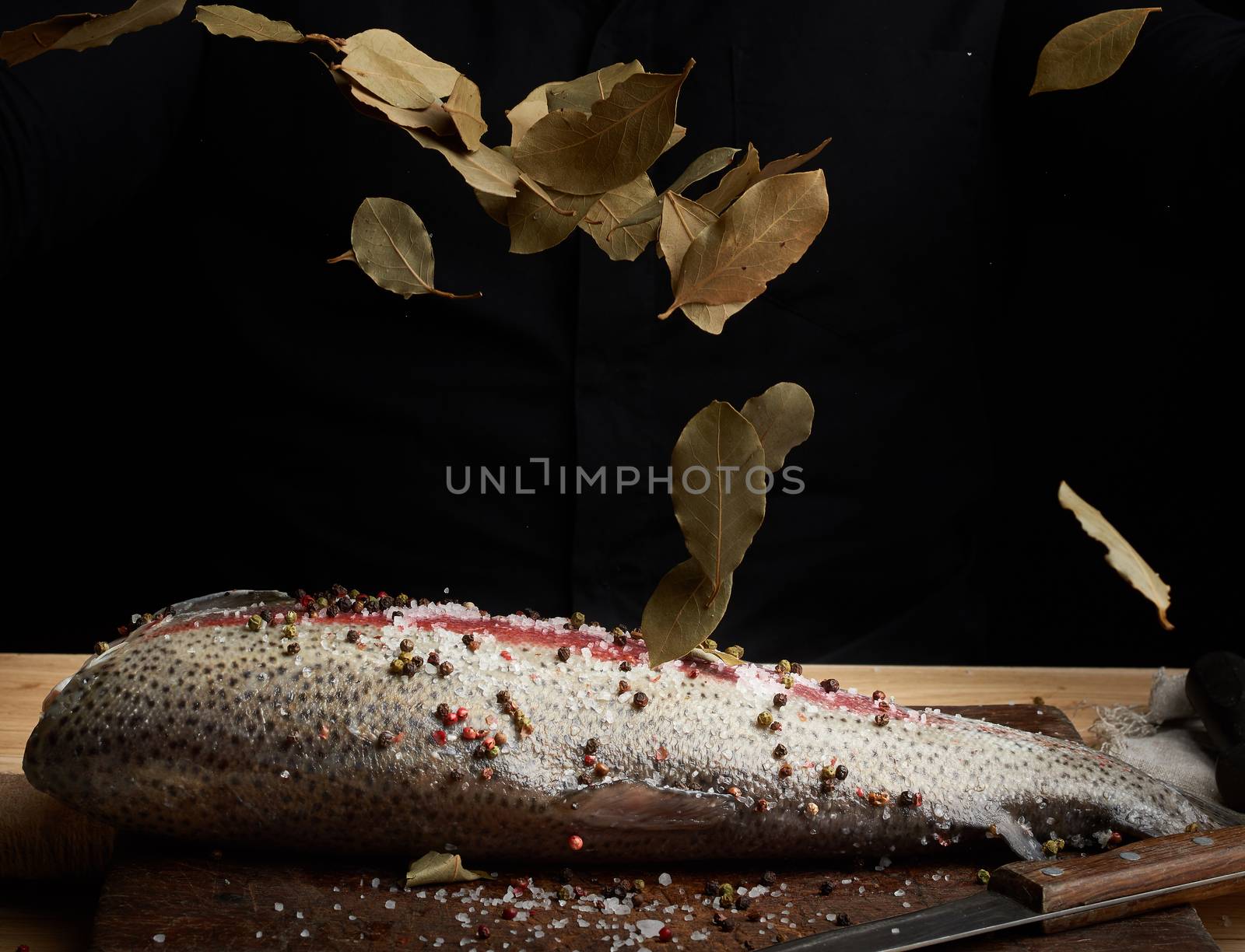 headless salmon filet on a wooden board sprinkled with leaves of dry bay leaves, process of cooking fish