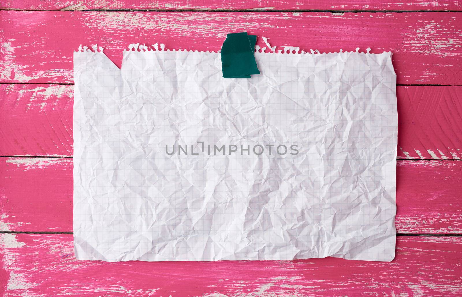 glued with adhesive tape rectangular empty white crumpled sheet of paper on a pink wooden background, place for inscription