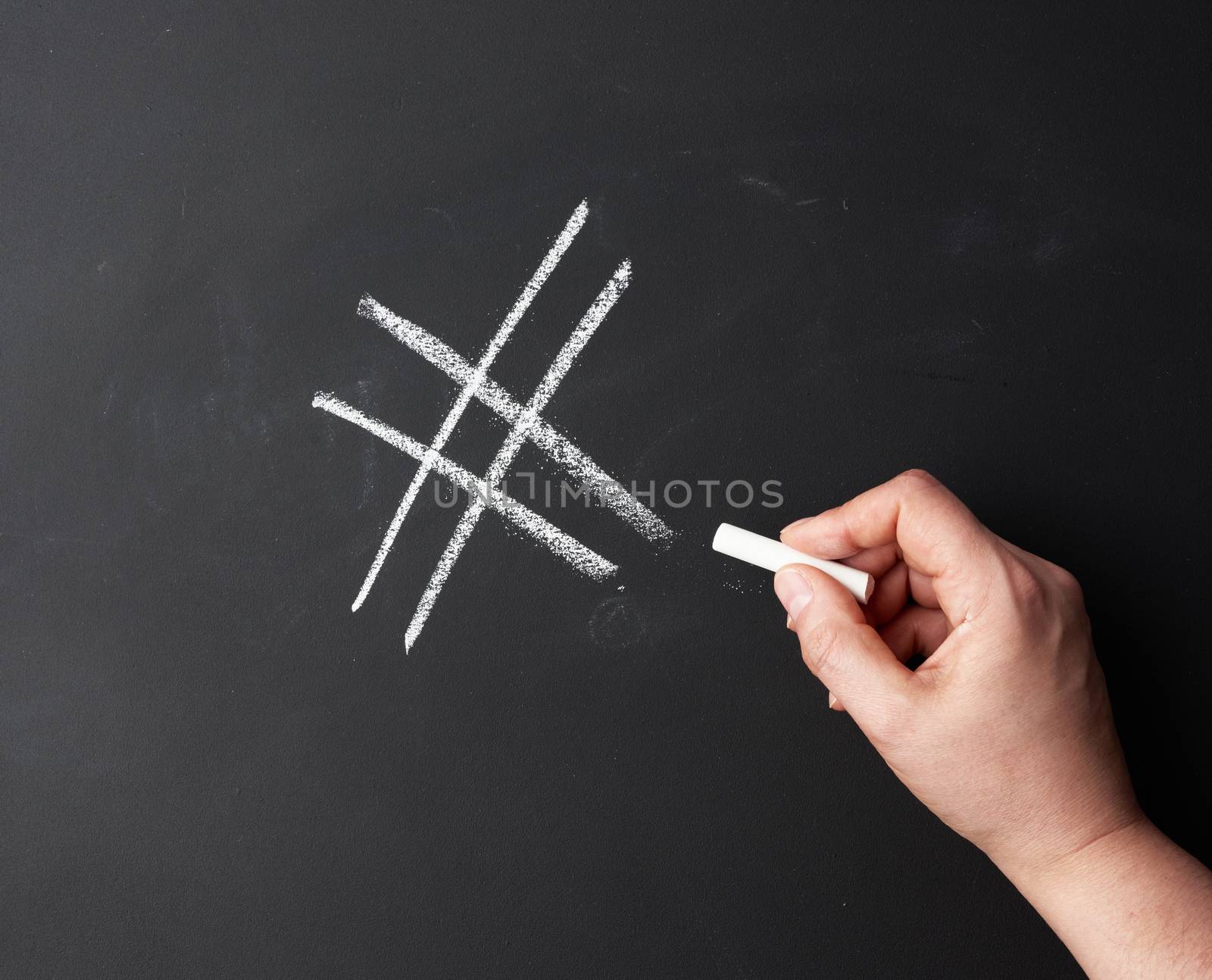 hand with chalk painted a hashtag on a black chalk board by ndanko