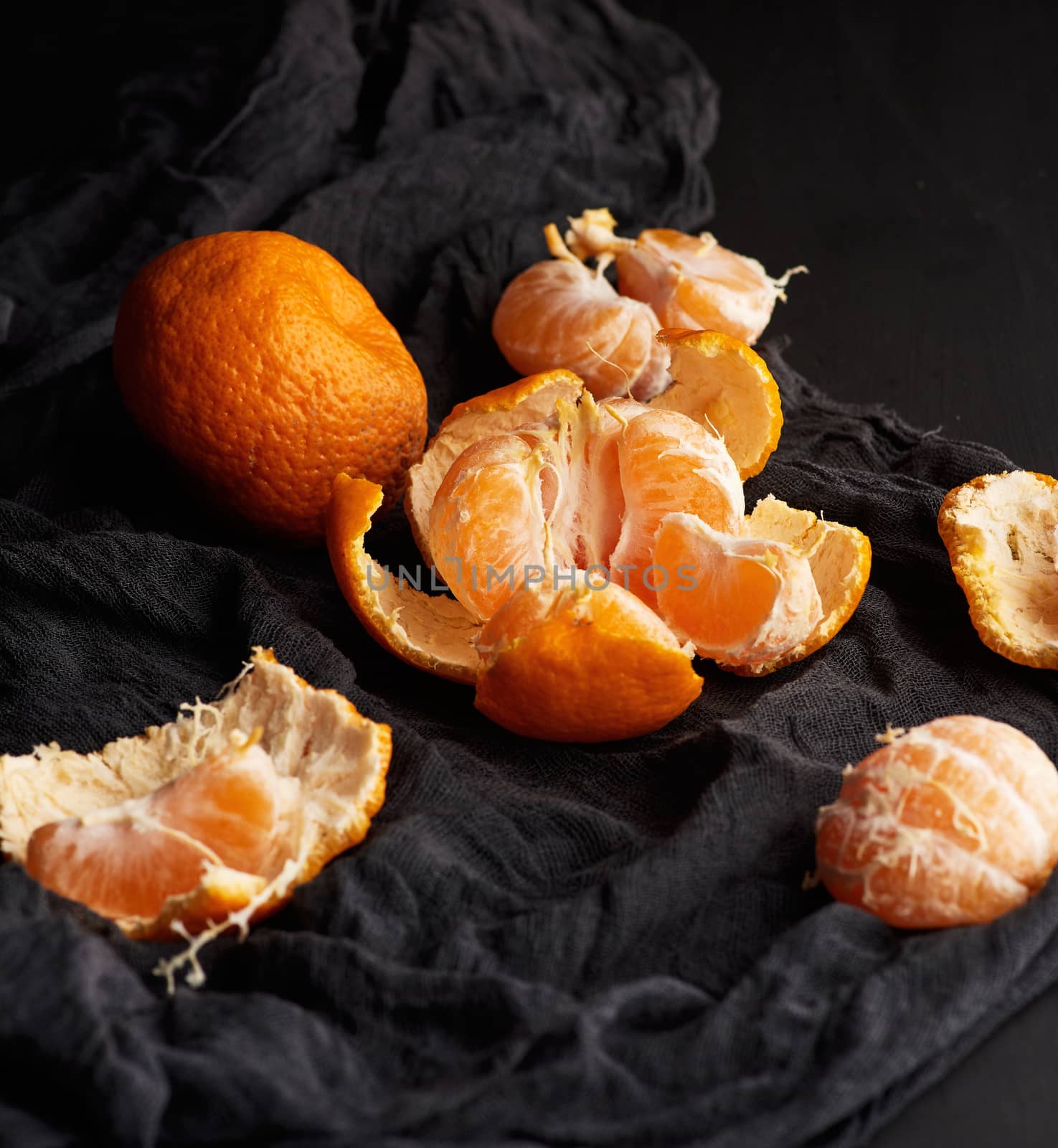 heap of unpeeled round ripe orange mandarin on a black napkin, wooden table, low key