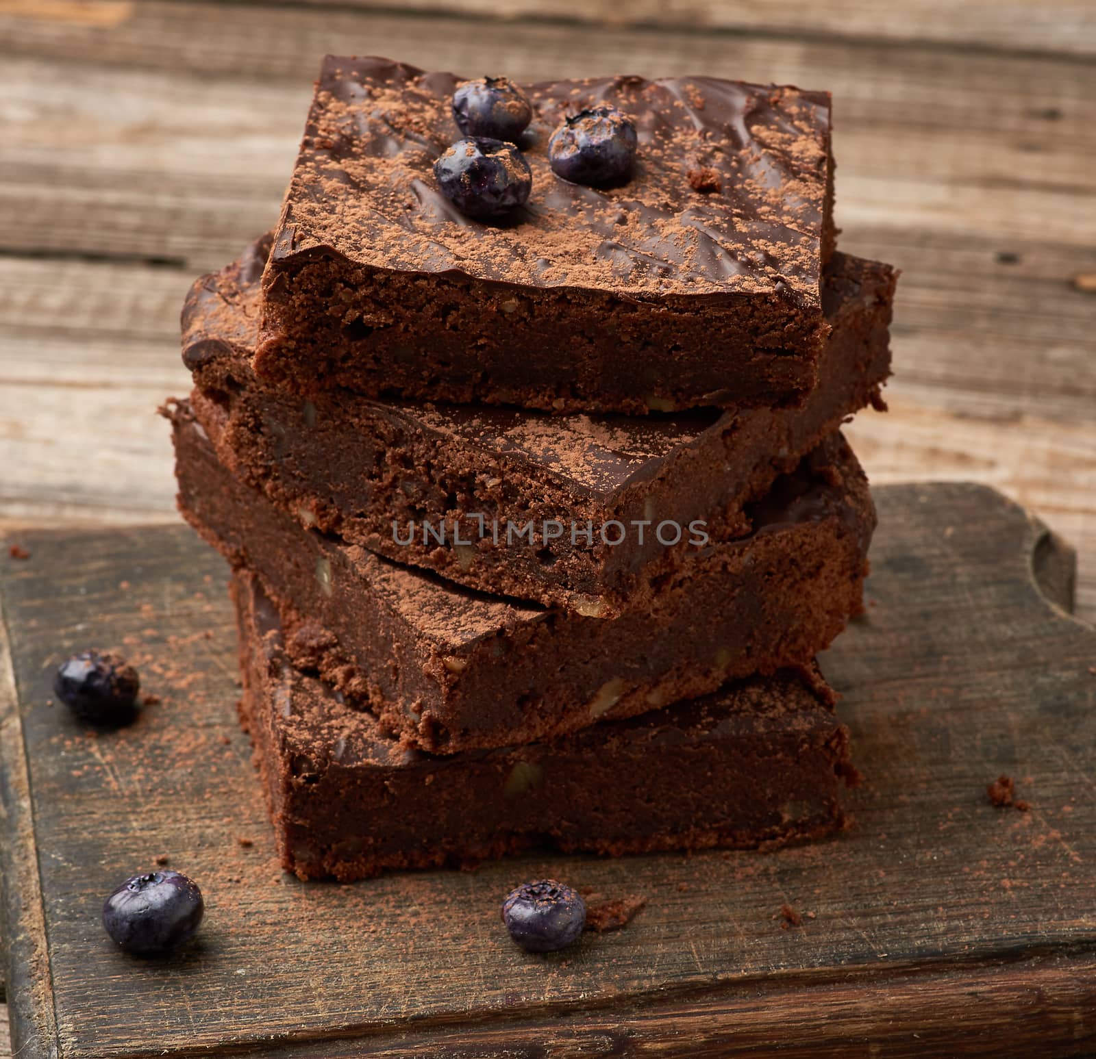 stack of square baked slices of brownie chocolate cake with walnuts on a wooden surface. Cooked homemade food. Chocolate pastry. Sweet meal, homemade dessert