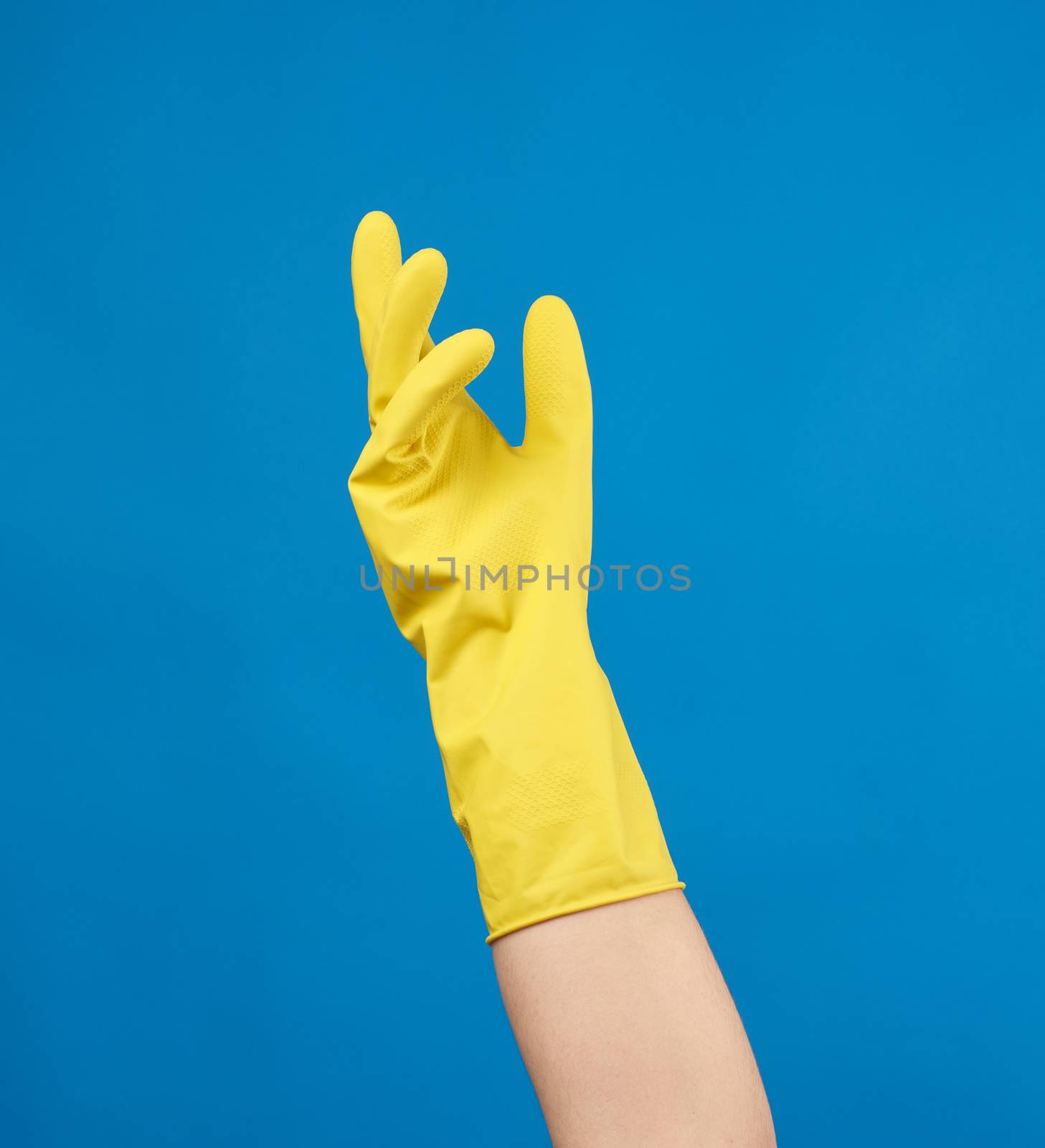 yellow rubber glove for cleaning dressed on a female hand, blue background, part of the body raised up