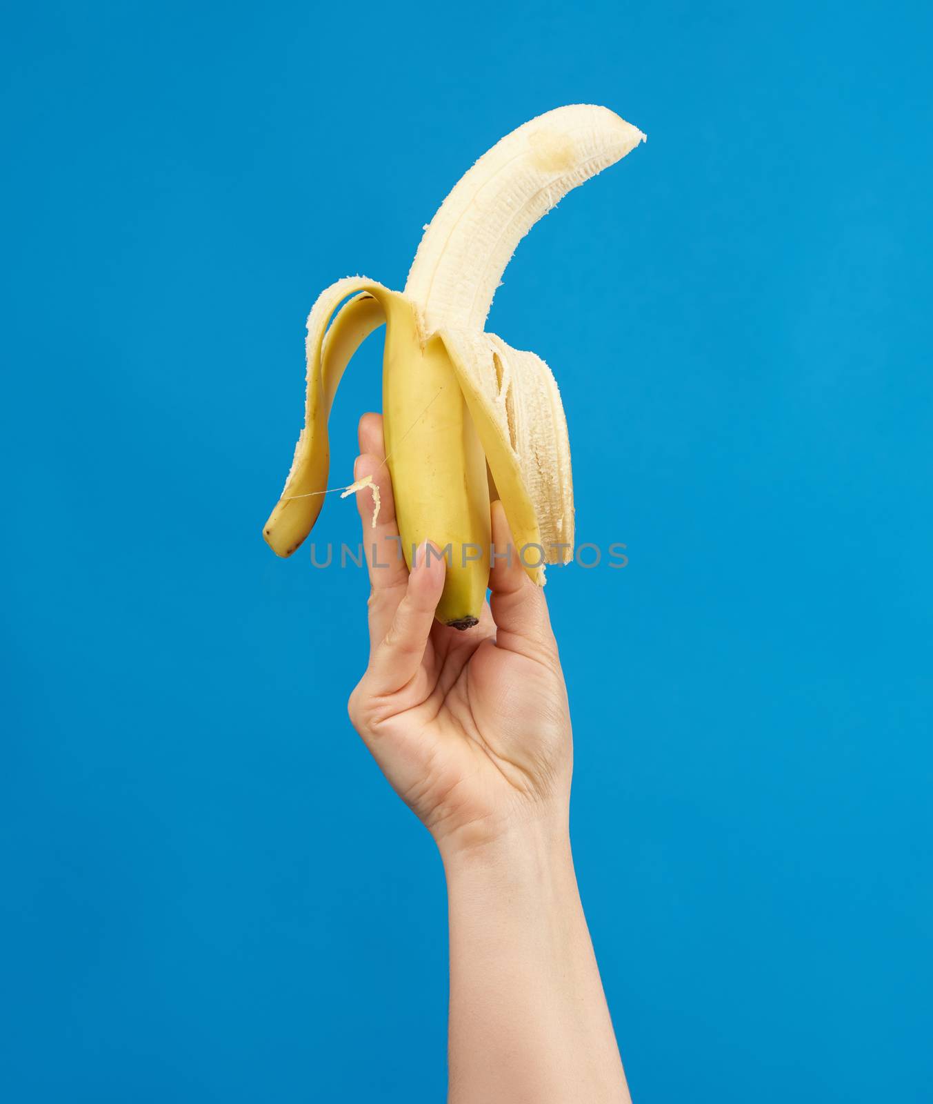 female hand holds a ripe peeled banana on a blue background by ndanko