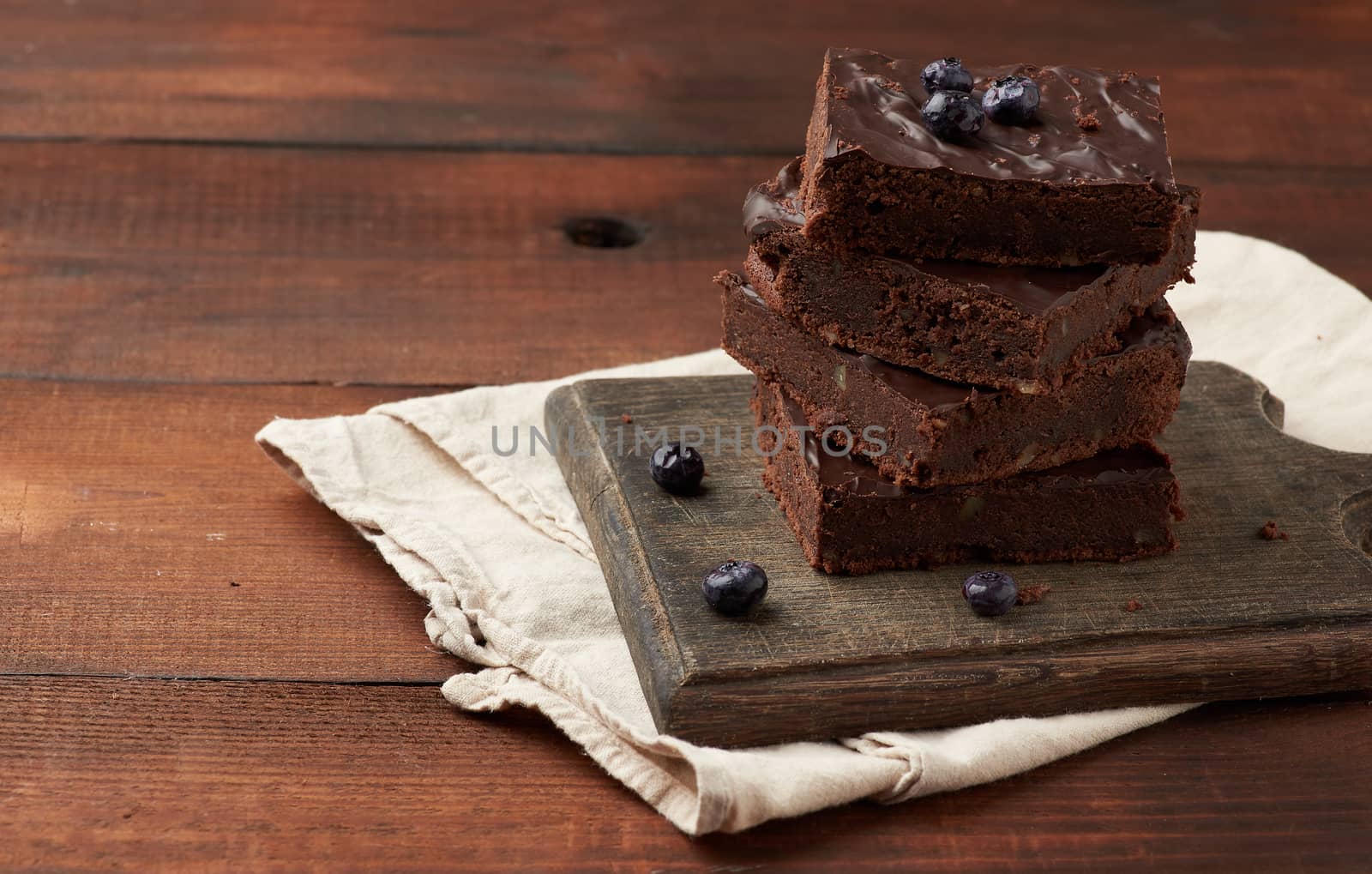 stack of square baked slices of brownie chocolate cake with walnuts on a wooden surface. Cooked homemade food. Chocolate pastry. Sweet meal, homemade dessert