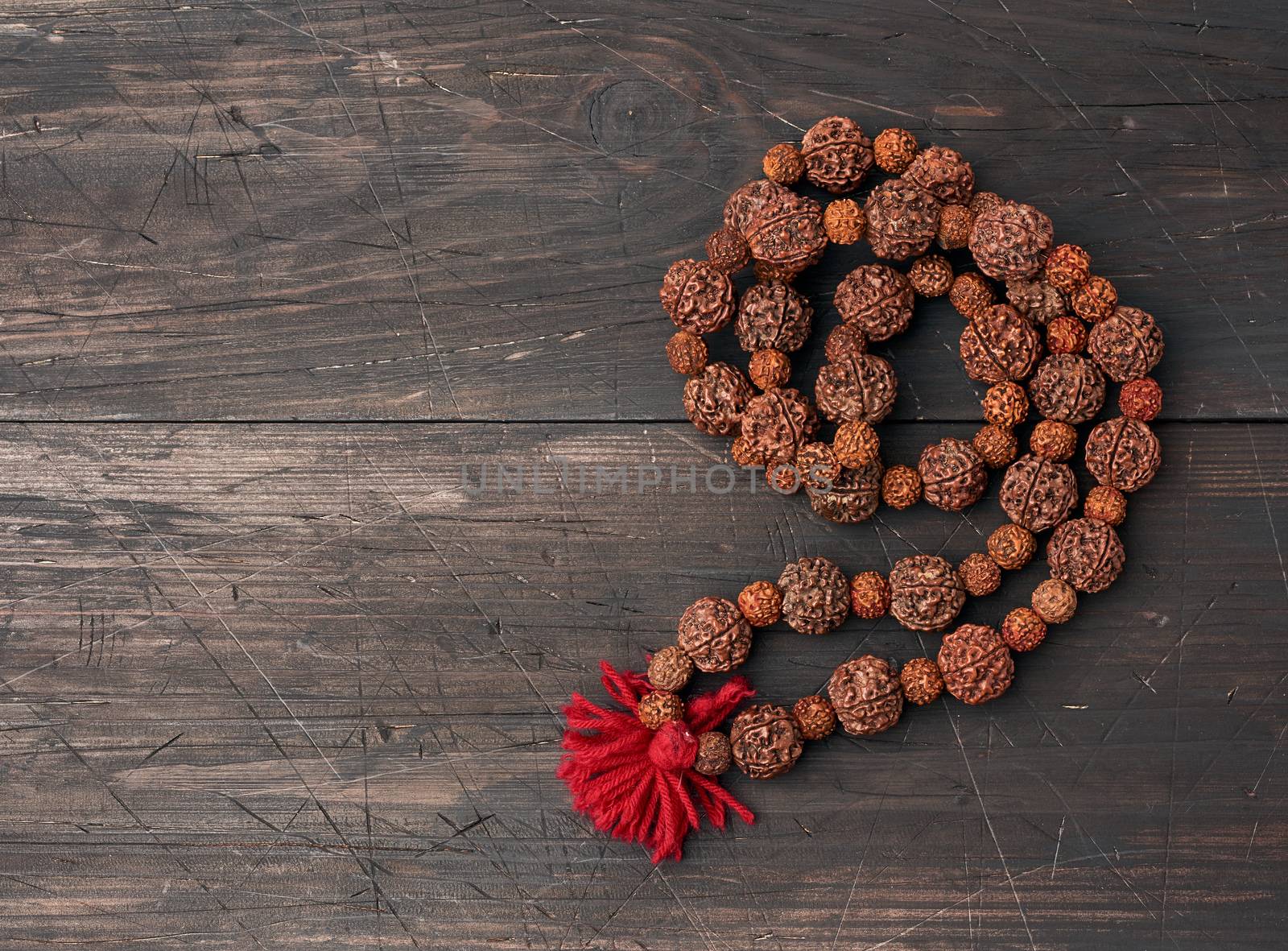 Rudraksha prayer beads for meditation on a brown wooden background, top view. Japa mala, copy space