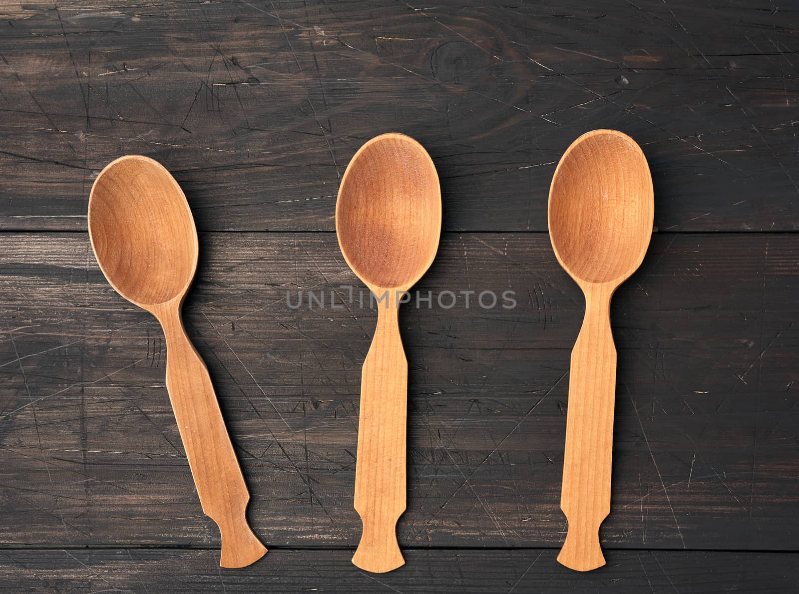 three empty wooden spoons on a brown wooden background from boards, top view